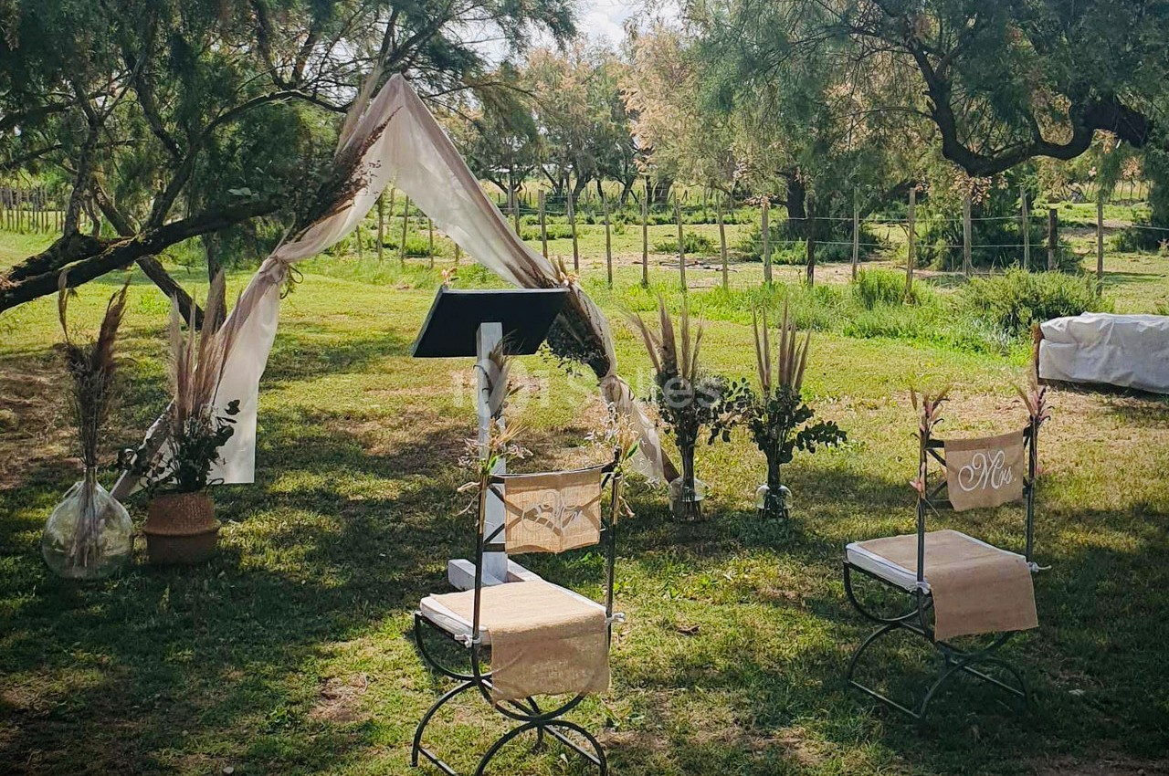 Chaises décorées et arche en tissu installées dans un jardin pour une cérémonie en plein air.
