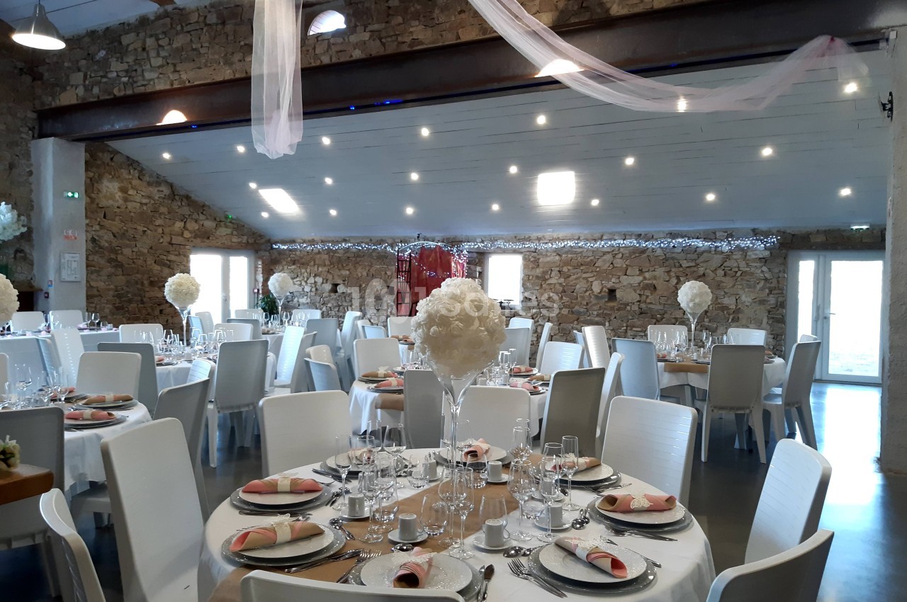 Salle de réception décorée avec des tables rondes dressées, nappes blanches et centres de table fleuris.