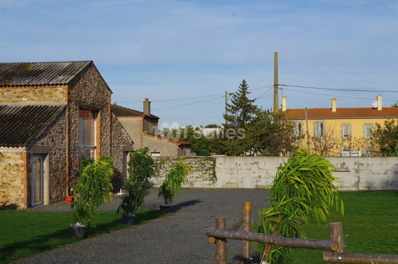 Cour extérieure avec des bâtiments en pierre, des plantes en pot et une clôture en bois, sous un ciel dégagé.