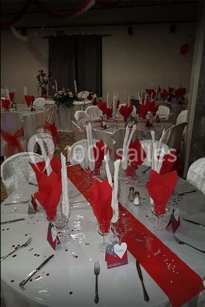 Salle décorée pour un événement avec des tables rondes ornées de nappes blanches, serviettes rouges et centres de table…
