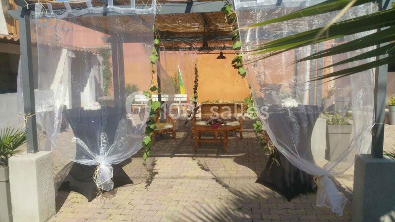 Espace extérieur décoré avec des voilages transparents, mobilier en bois et plantes grimpantes sous une pergola.