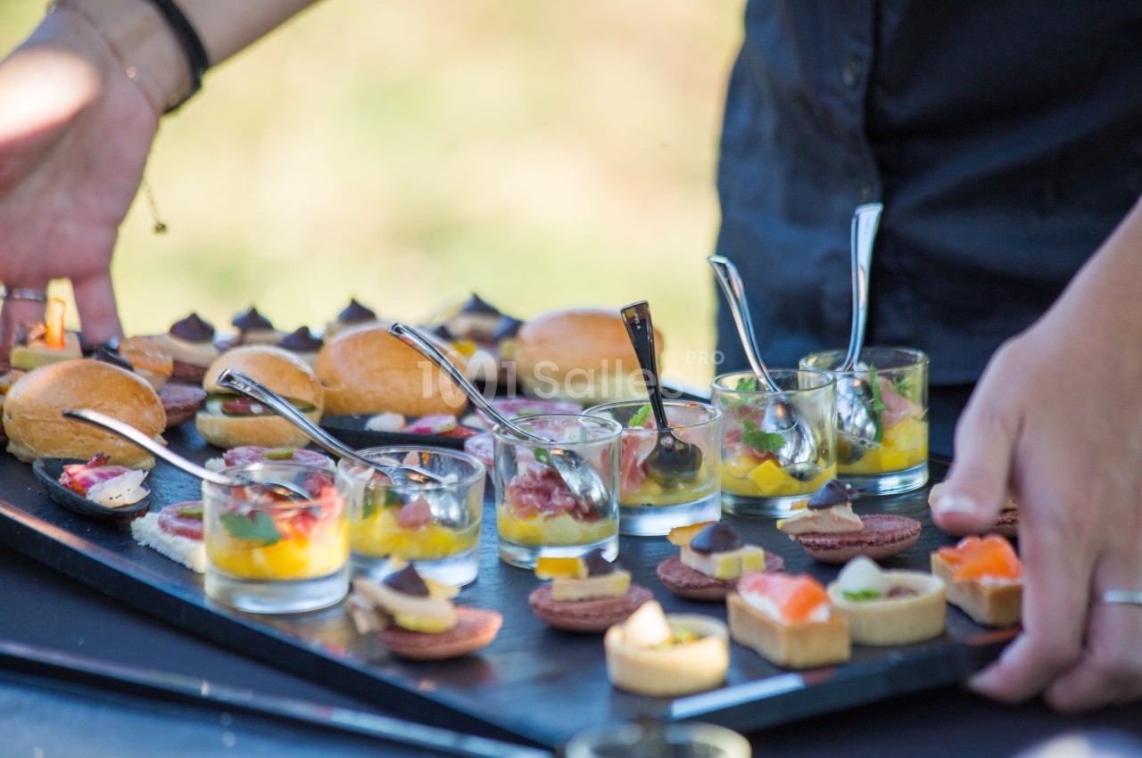 Plateau de verrines et amuse-bouches variés disposés sur une table, avec des mains en train de les arranger.