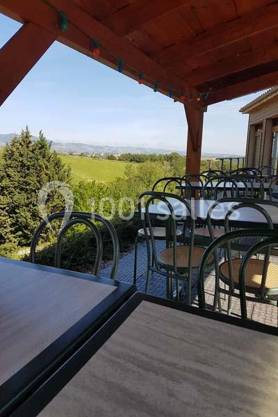 Terrasse couverte avec tables et chaises en métal, offrant une vue sur un paysage verdoyant et dégagé.
