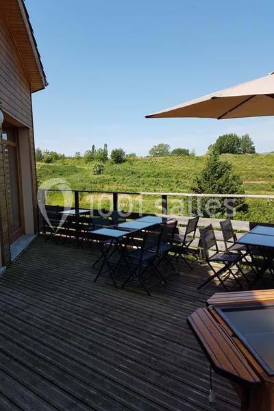 Terrasse en bois avec tables et chaises noires, vue sur un paysage verdoyant sous un ciel bleu dégagé.