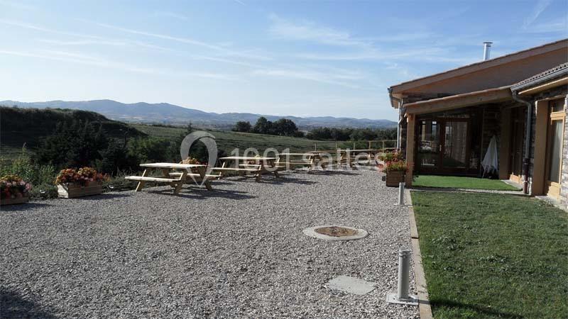 Terrasse en gravier avec tables de pique-nique, vue sur un paysage vallonné sous un ciel dégagé.