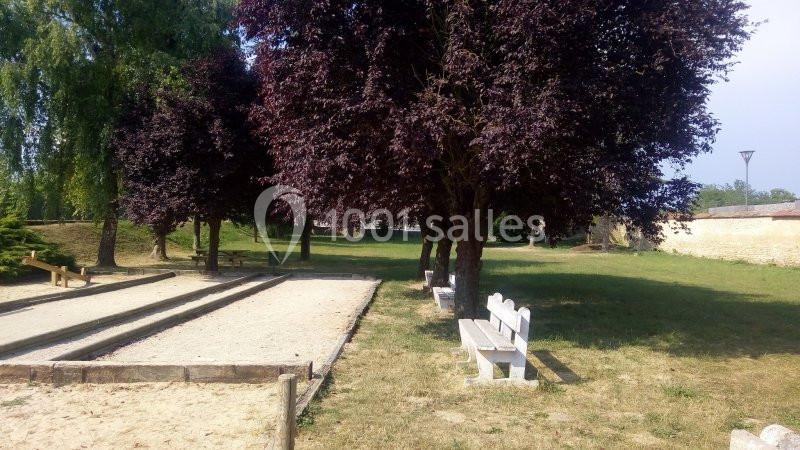 Allée avec bancs, terrain de pétanque et arbres ombragés dans un parc ensoleillé.