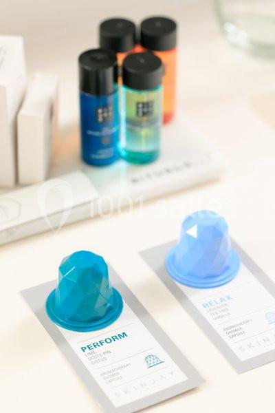 Capsules de soin bleu et turquoise avec des flacons de produits cosmétiques en arrière-plan sur une surface claire.