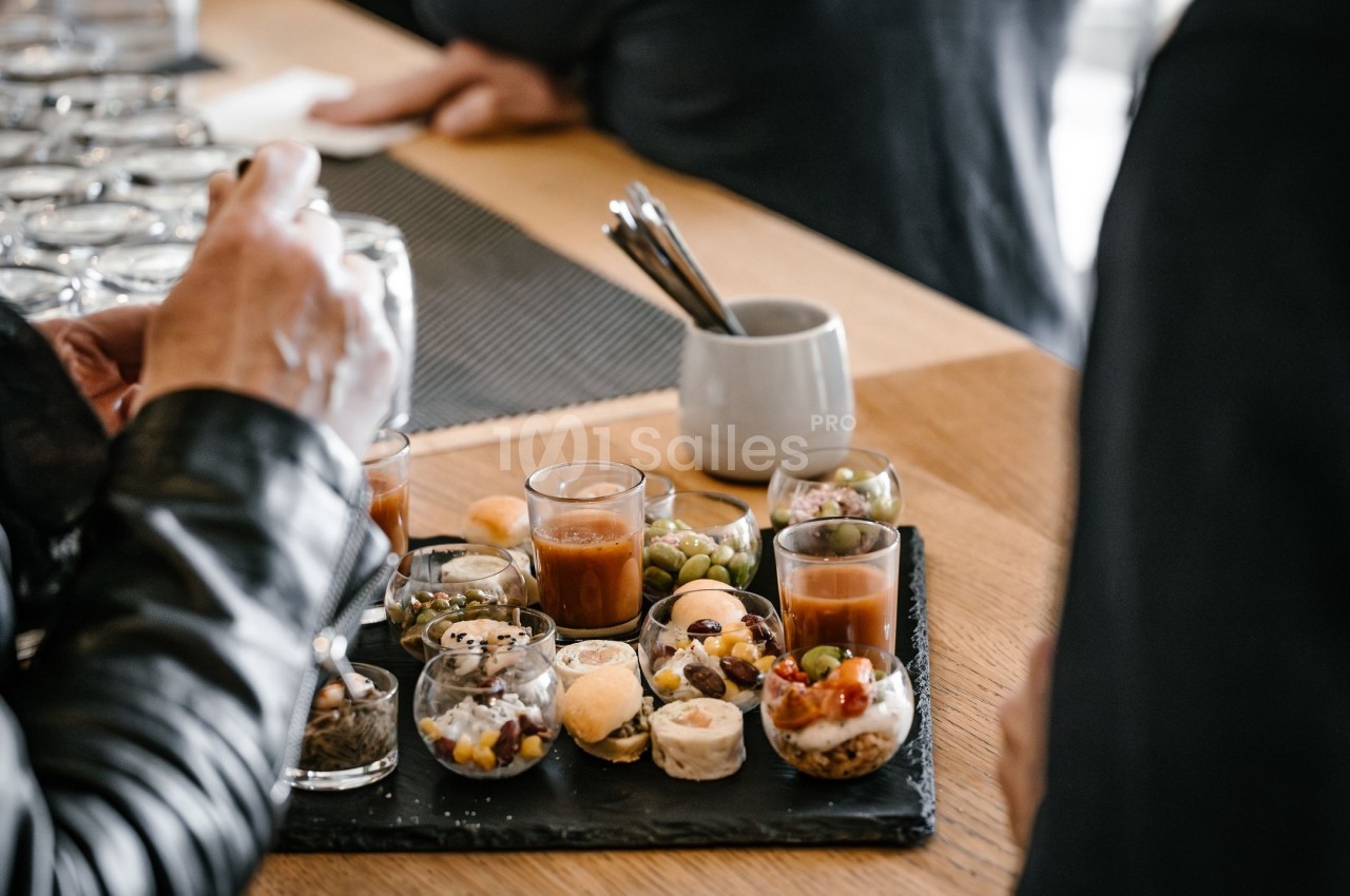 Plateau d'amuse-bouches variés avec verrines, macarons salés et olives, posé sur une table en bois.