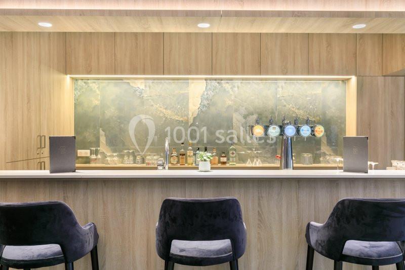 Bar moderne avec comptoir en marbre, tabourets noirs, étagères de bouteilles et robinets de bière alignés.
