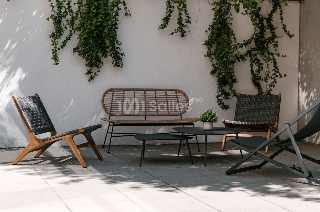 Mobilier de jardin en bois et rotin avec table basse, disposé sur une terrasse ensoleillée, entourée de plantes grimpantes.