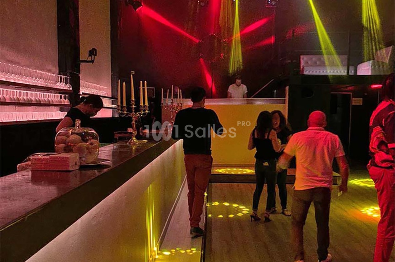 Intérieur d'une discothèque avec bar éclairé, lumières rouges et jaunes, et quelques personnes dansant ou discutant.