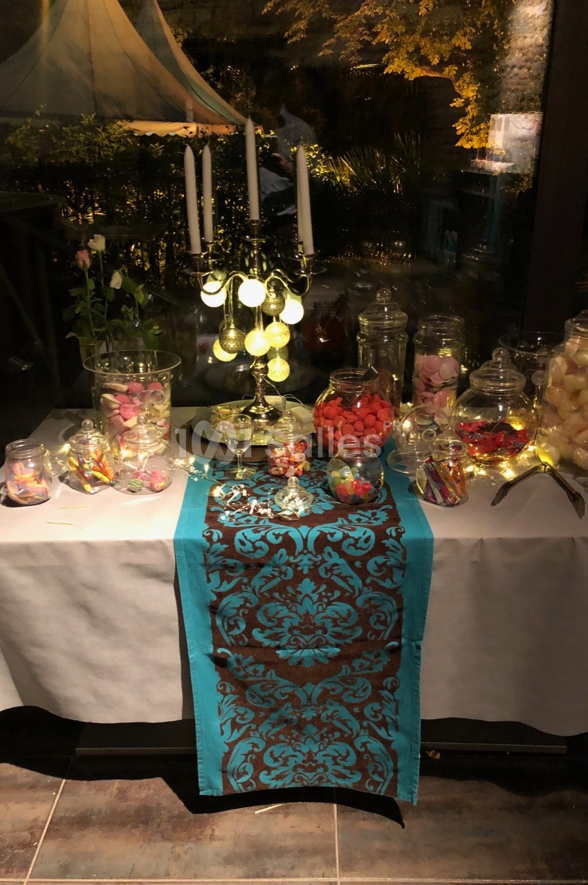 Table décorée avec un chemin de table turquoise, des bonbonnières remplies de sucreries et un chandelier allumé.