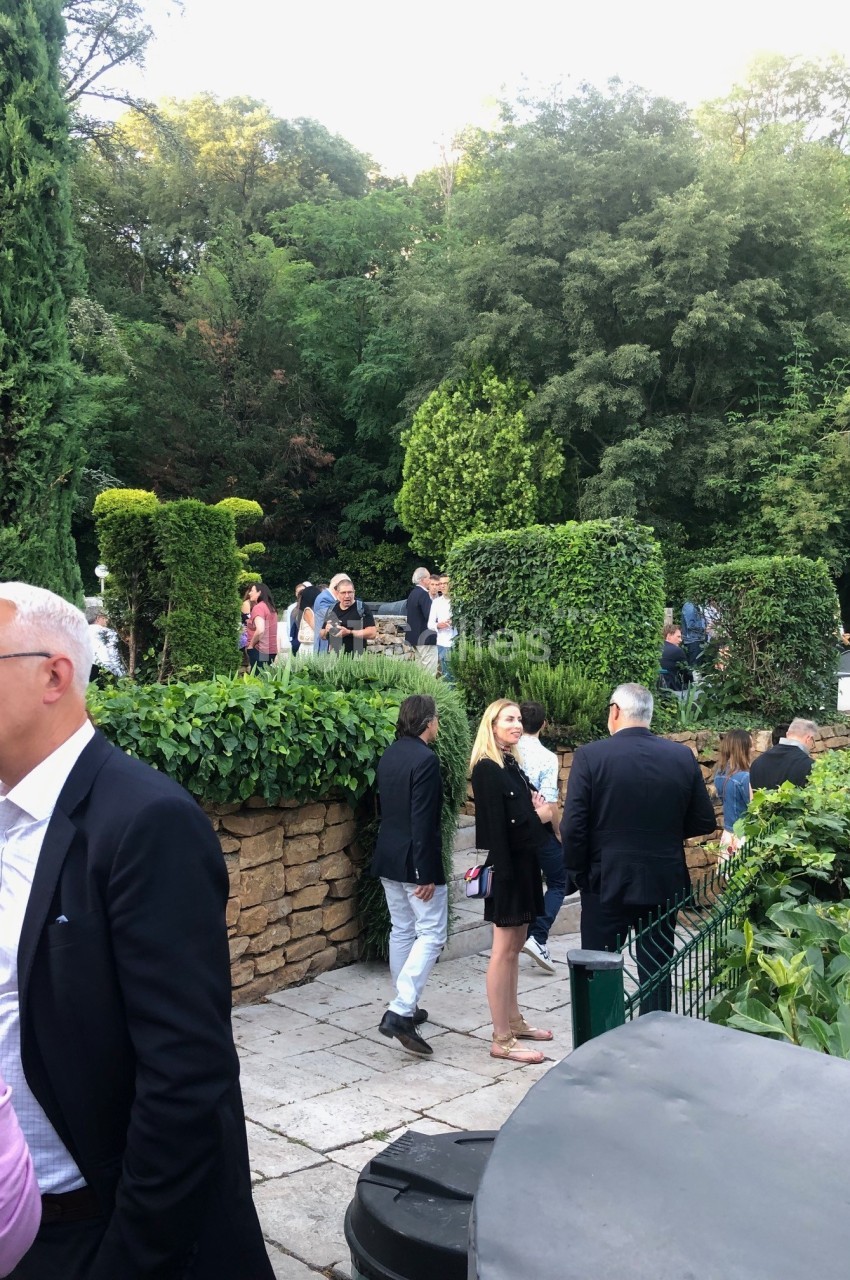 Personnes discutant dans un jardin aménagé avec des haies et des arbres en arrière-plan.