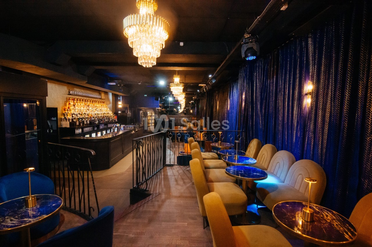 Salle de bar élégante avec des fauteuils colorés, des tables en marbre bleu et des lustres suspendus.