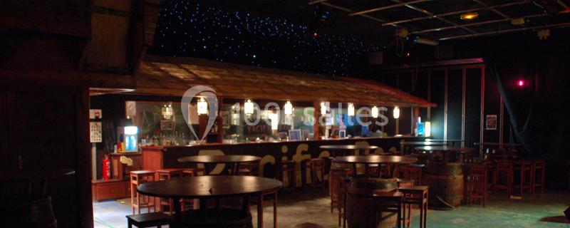 Bar en intérieur avec comptoir en bois, tabourets et tables rondes, éclairage tamisé et plafond étoilé.