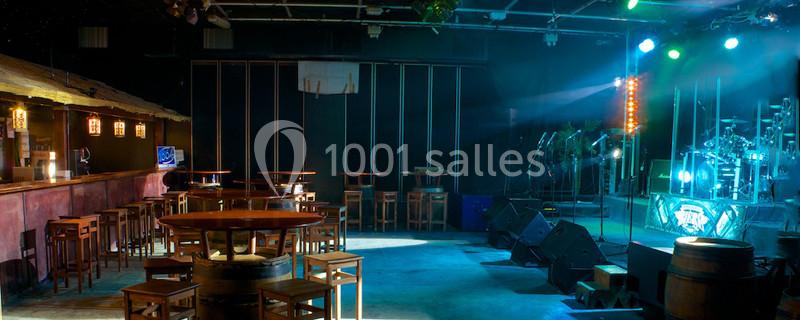 Salle de concert vide avec scène éclairée, instruments de musique et tables en bois disposées autour d'un bar.