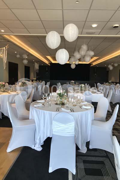 Salle de réception décorée avec des tables rondes dressées, nappes blanches et lanternes suspendues au plafond.