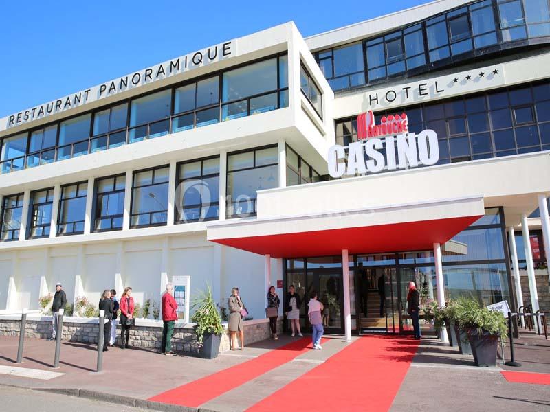Façade d'un bâtiment moderne abritant un casino, un hôtel et un restaurant, avec un tapis rouge à l'entrée.