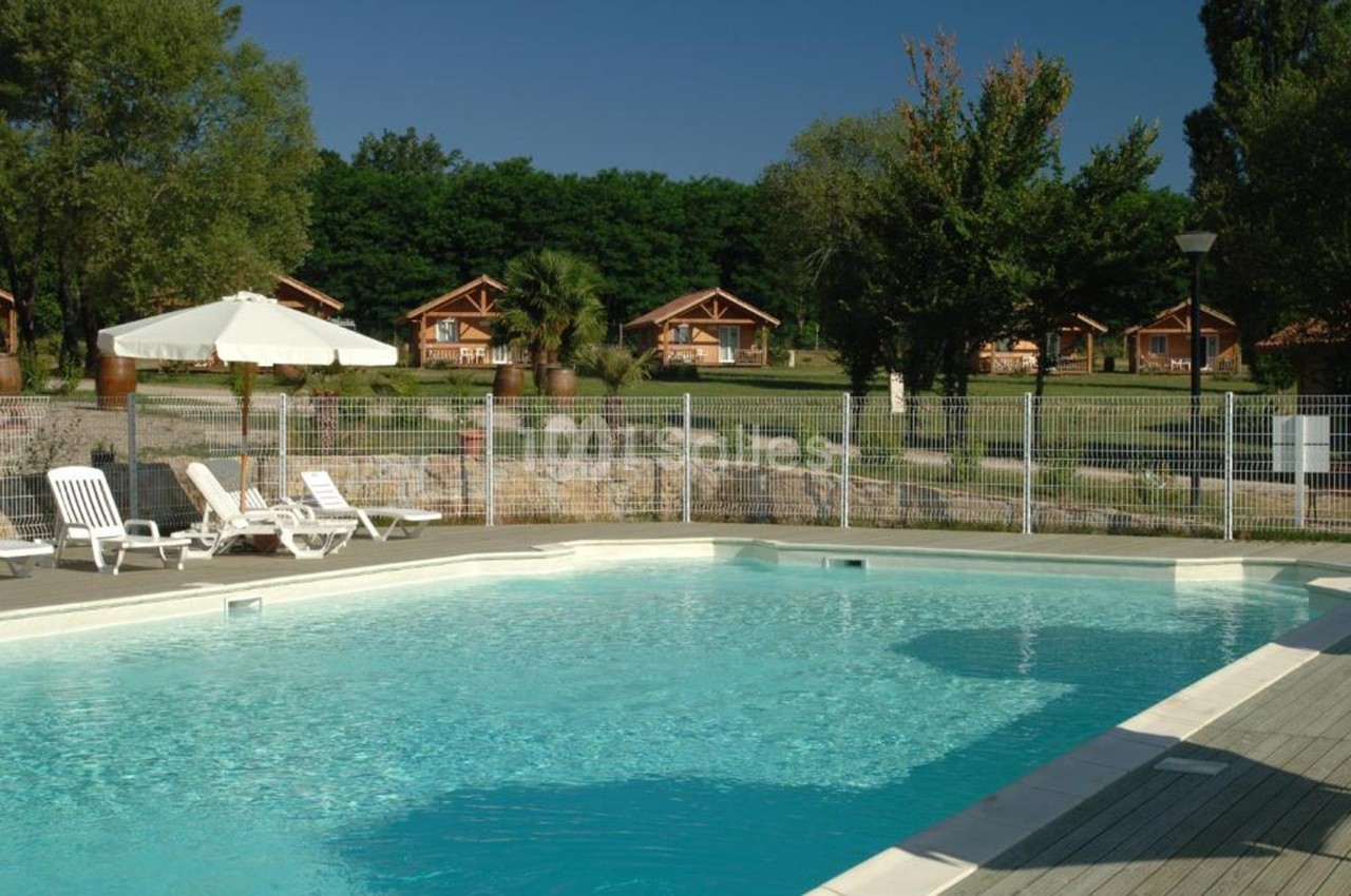Piscine extérieure entourée de chaises longues, parasols et vue sur des chalets en bois dans un cadre verdoyant.