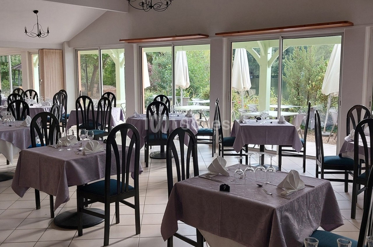 Salle de restaurant lumineuse avec tables dressées, nappes violettes et vue sur une terrasse extérieure verdoyante.