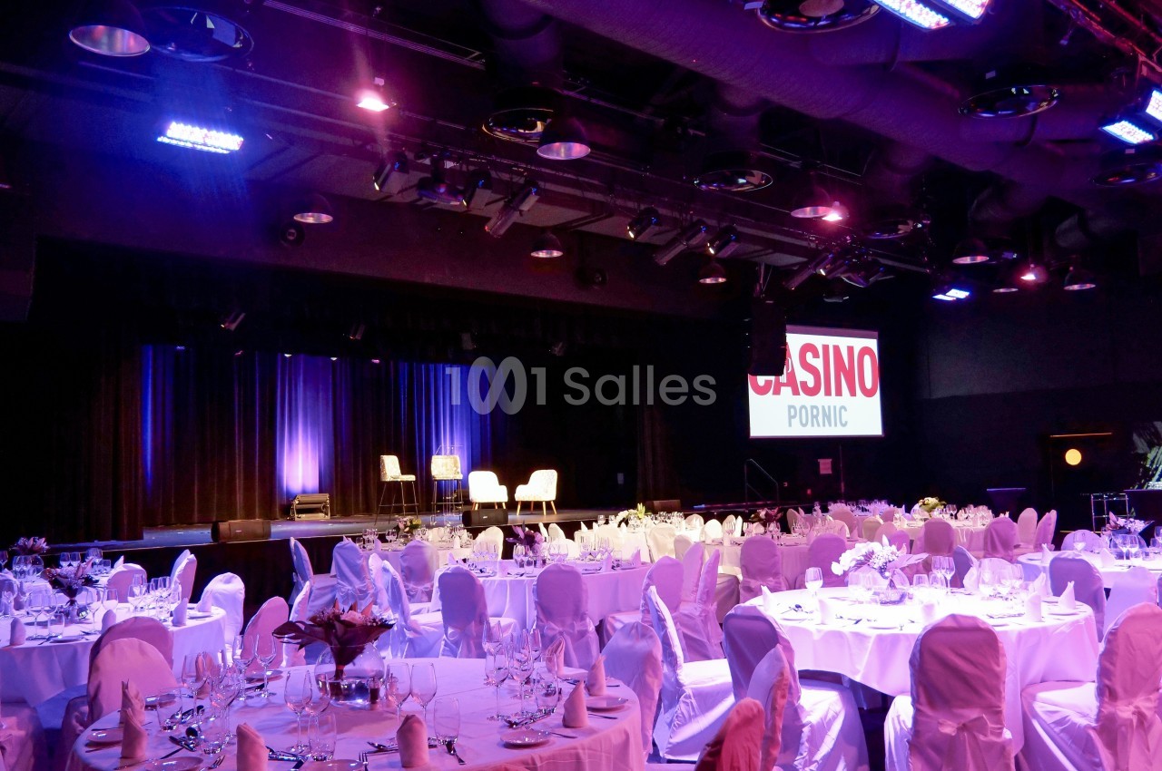 Salle de réception avec tables dressées, éclairage coloré et scène en arrière-plan portant l'inscription ’Casino Pornic’.
