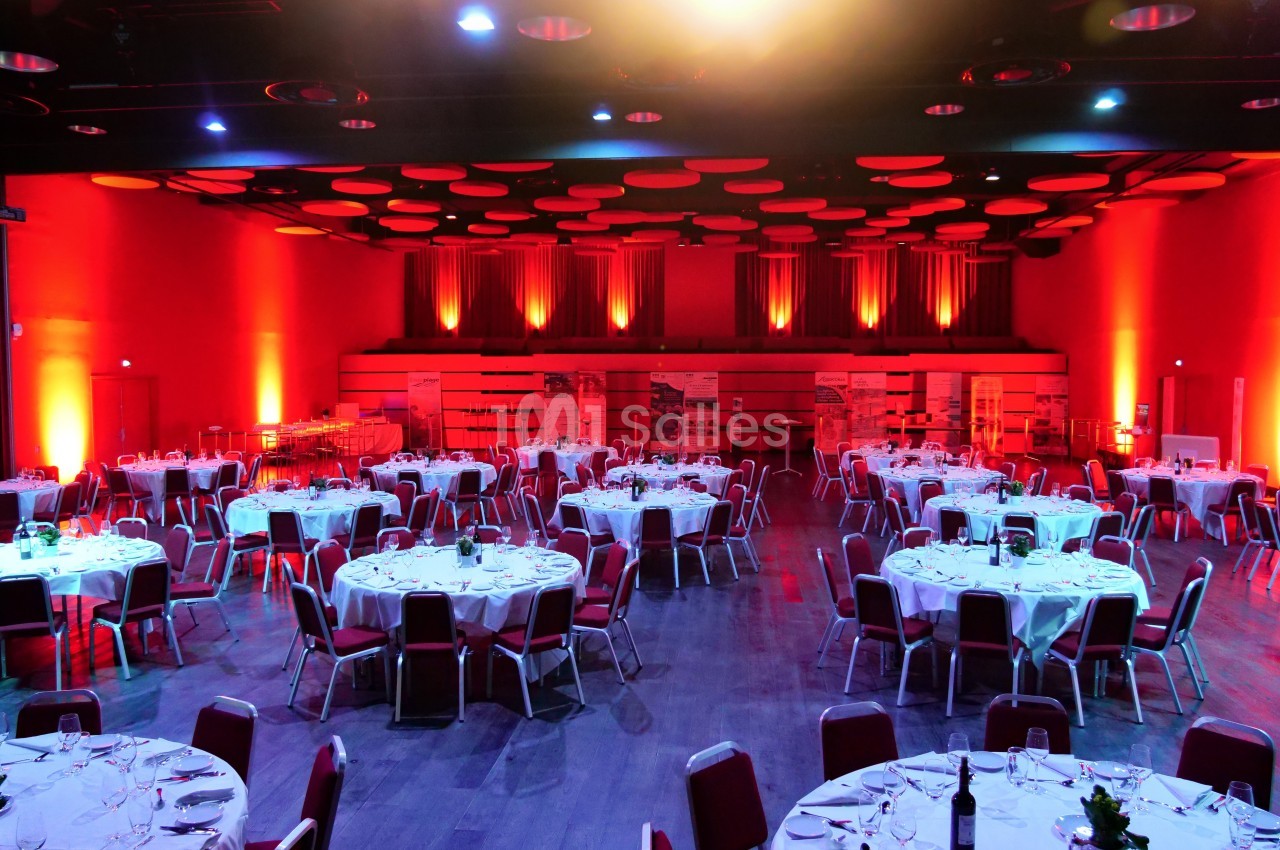 Salle de réception éclairée en rouge avec des tables rondes dressées pour un événement.