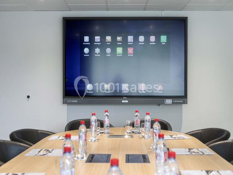 Écran interactif affichant des icônes d'applications, installé dans une salle de réunion avec table et bouteilles d'eau.