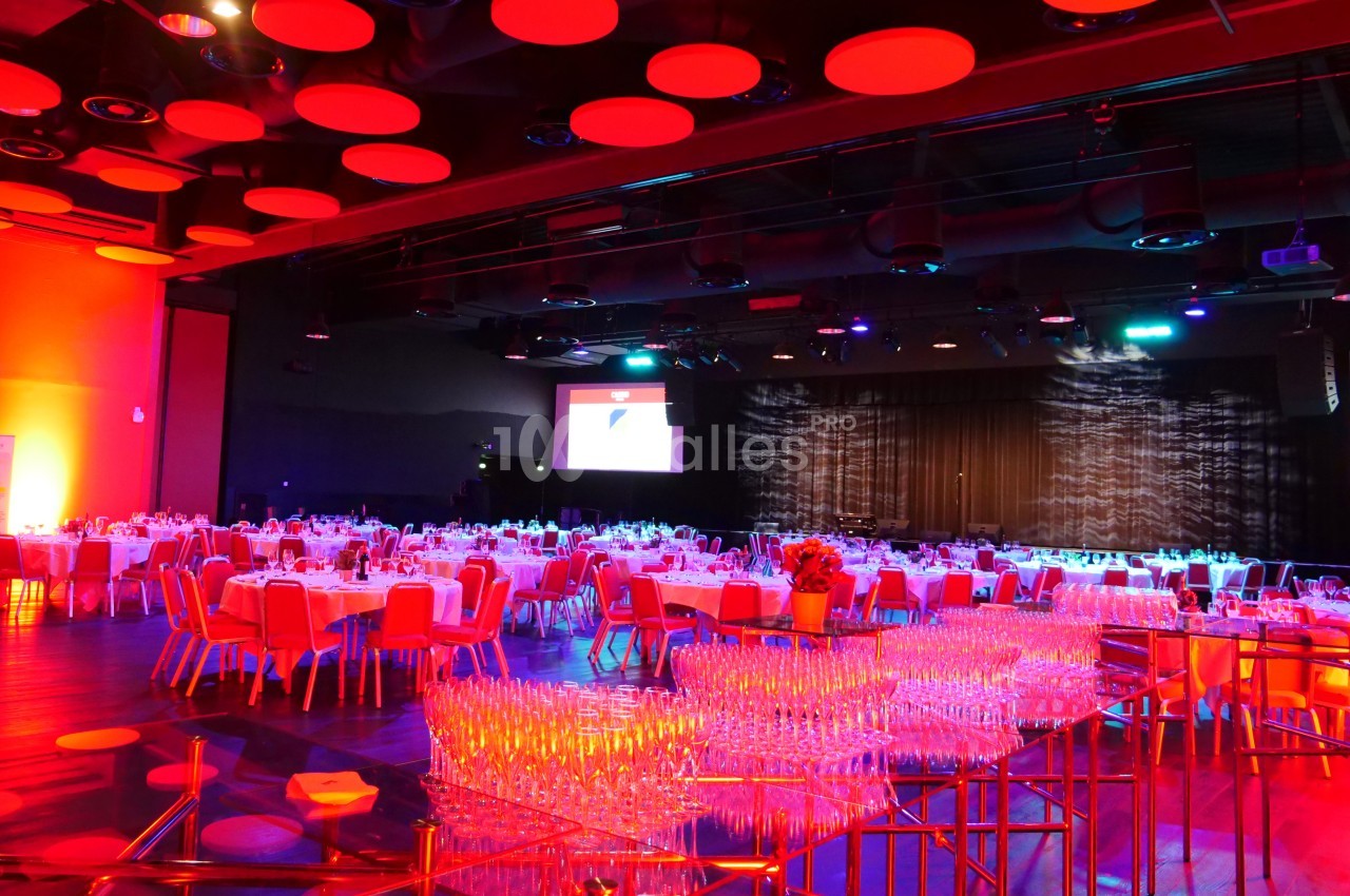 Salle de réception avec tables dressées, éclairage rouge et écran de projection en arrière-plan.