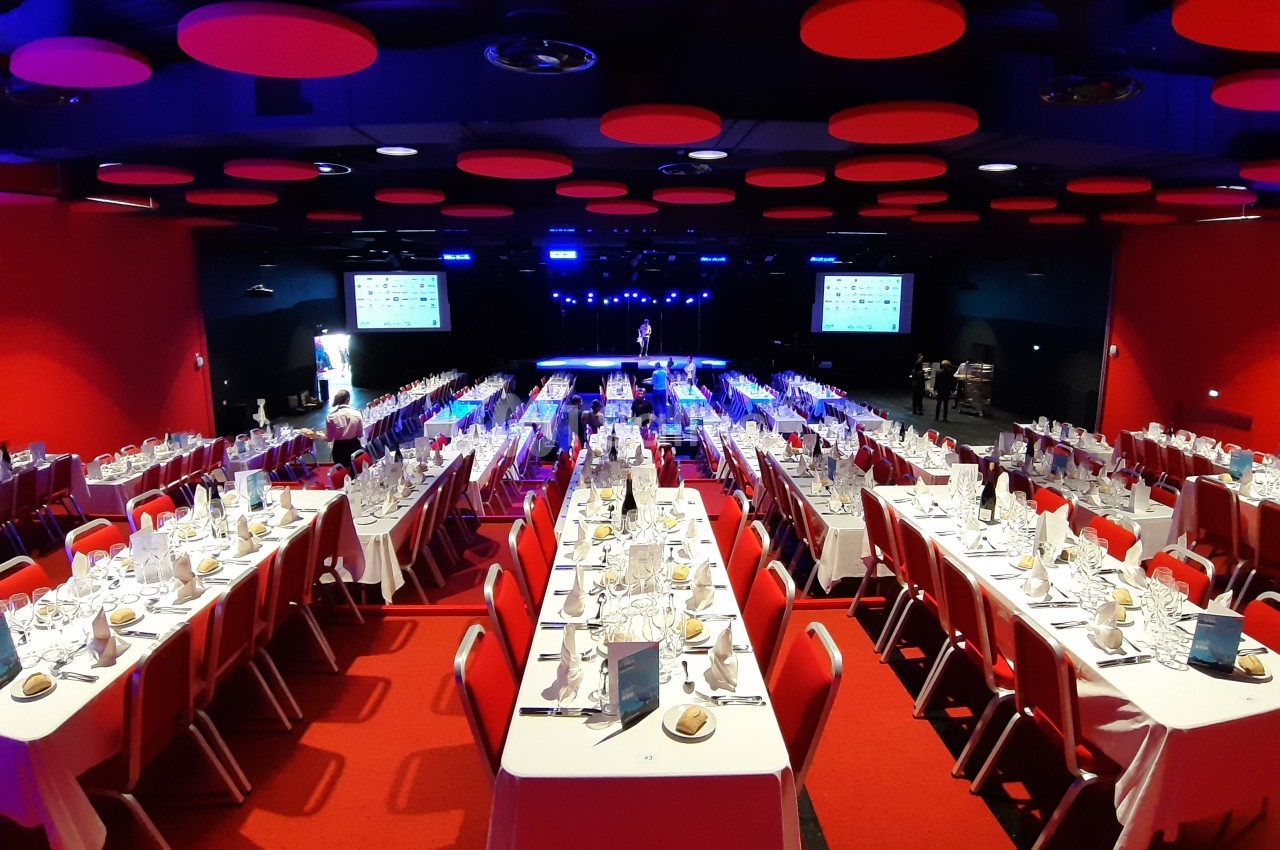 Salle de réception avec des tables dressées pour un dîner, éclairage tamisé et décorations rouges au plafond.