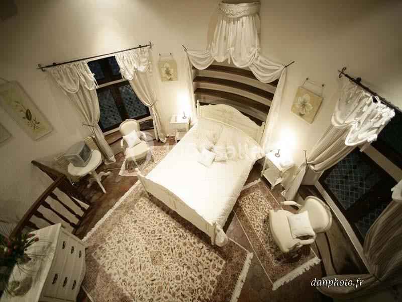 Chambre lumineuse avec lit double, mobilier blanc, tapis décoratif et fenêtres encadrées de rideaux élégants.