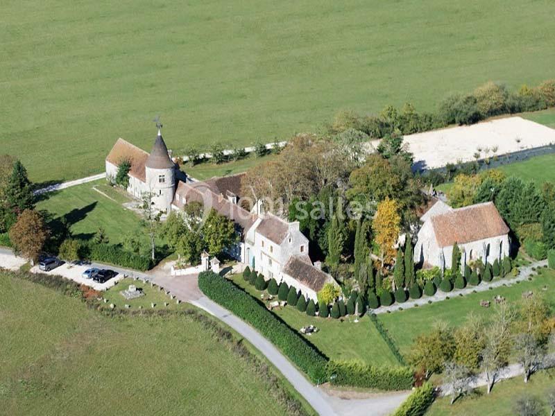 Vue aérienne d'un domaine rural avec bâtiments anciens, une tour, jardins aménagés et champs environnants.