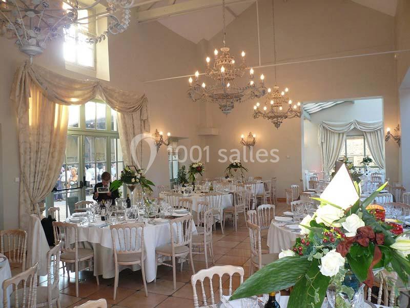 Salle de réception élégante avec tables dressées, chaises en bois clair, lustres et décorations florales.