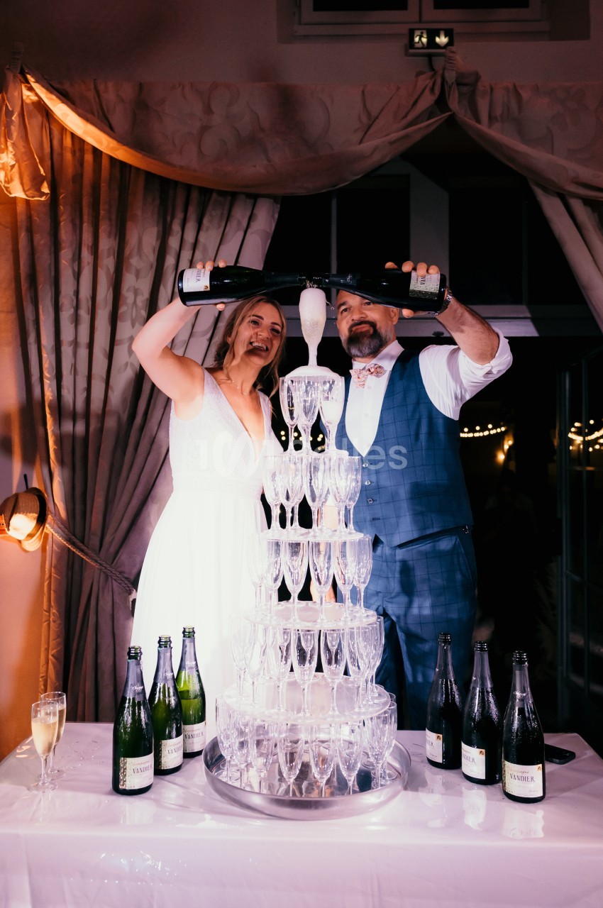 Un couple verse du champagne dans une pyramide de flûtes lors d'une célébration festive en intérieur.