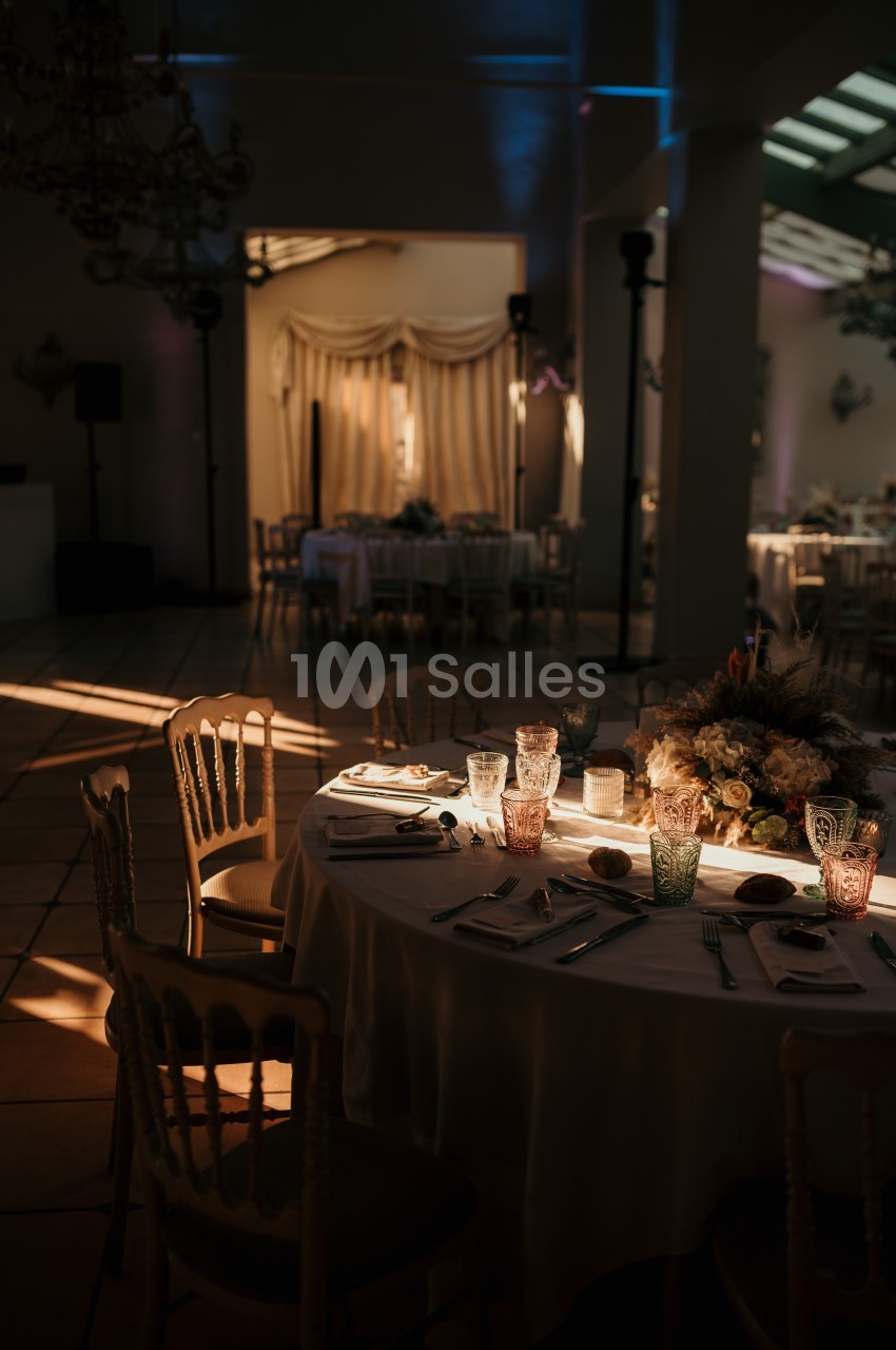 Salle de réception éclairée par une lumière tamisée, table dressée avec vaisselle et décoration florale.
