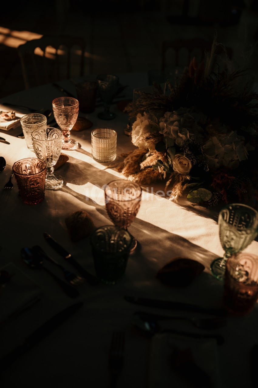 Table décorée avec des verres colorés, des couverts et un centre de table floral, éclairée par une lumière douce.