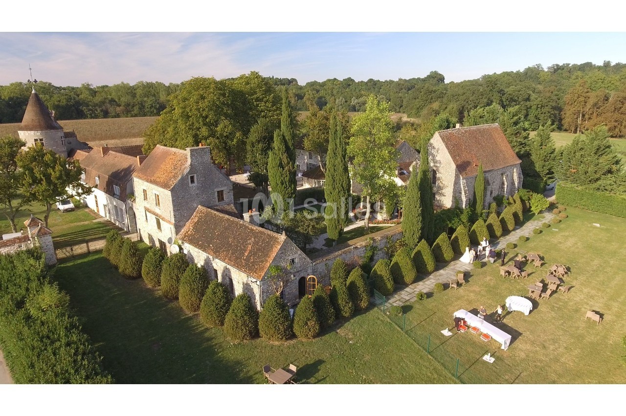 Vue aérienne d'un domaine avec bâtiments en pierre, toits en tuiles, jardins arborés et espaces aménagés en plein air.