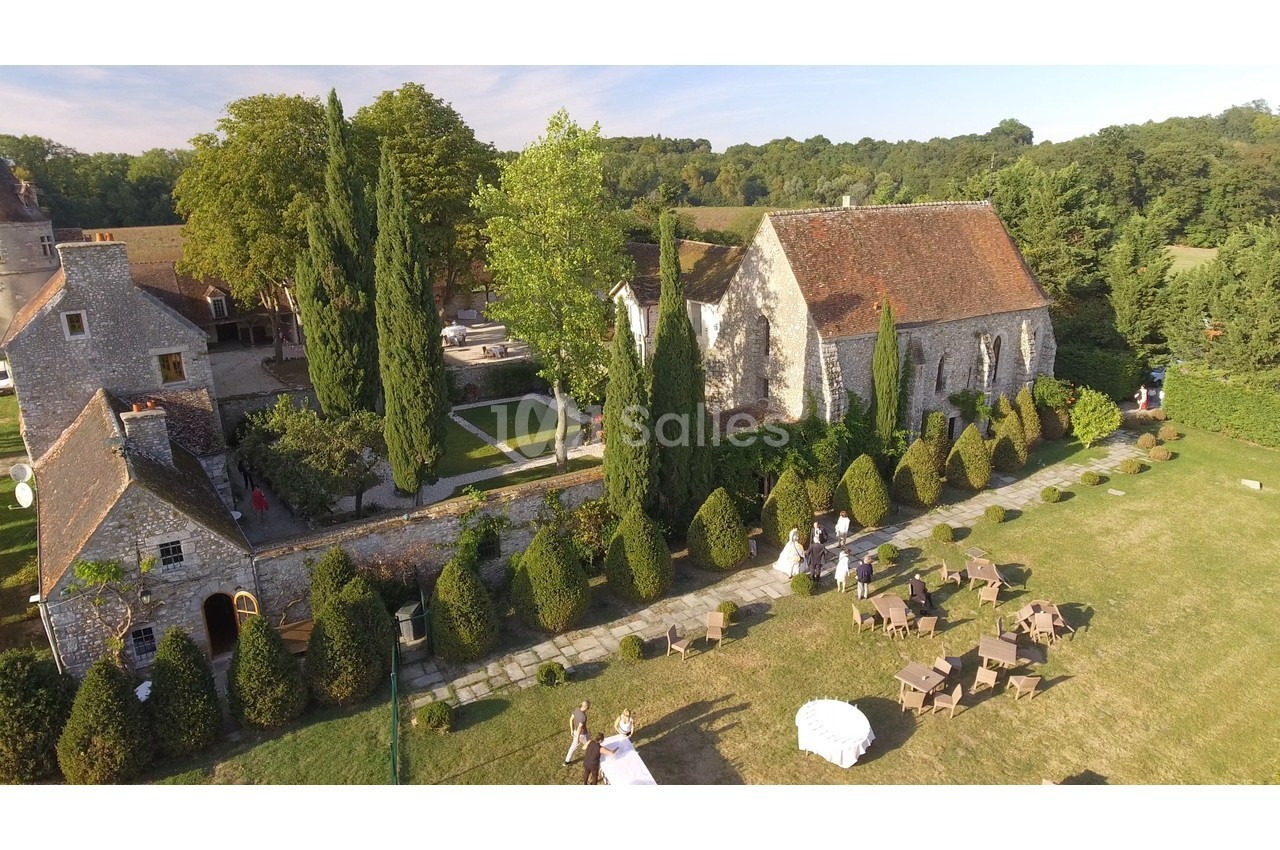 Vue aérienne d'un domaine avec une chapelle en pierre, des jardins aménagés et des tables installées sur la pelouse.