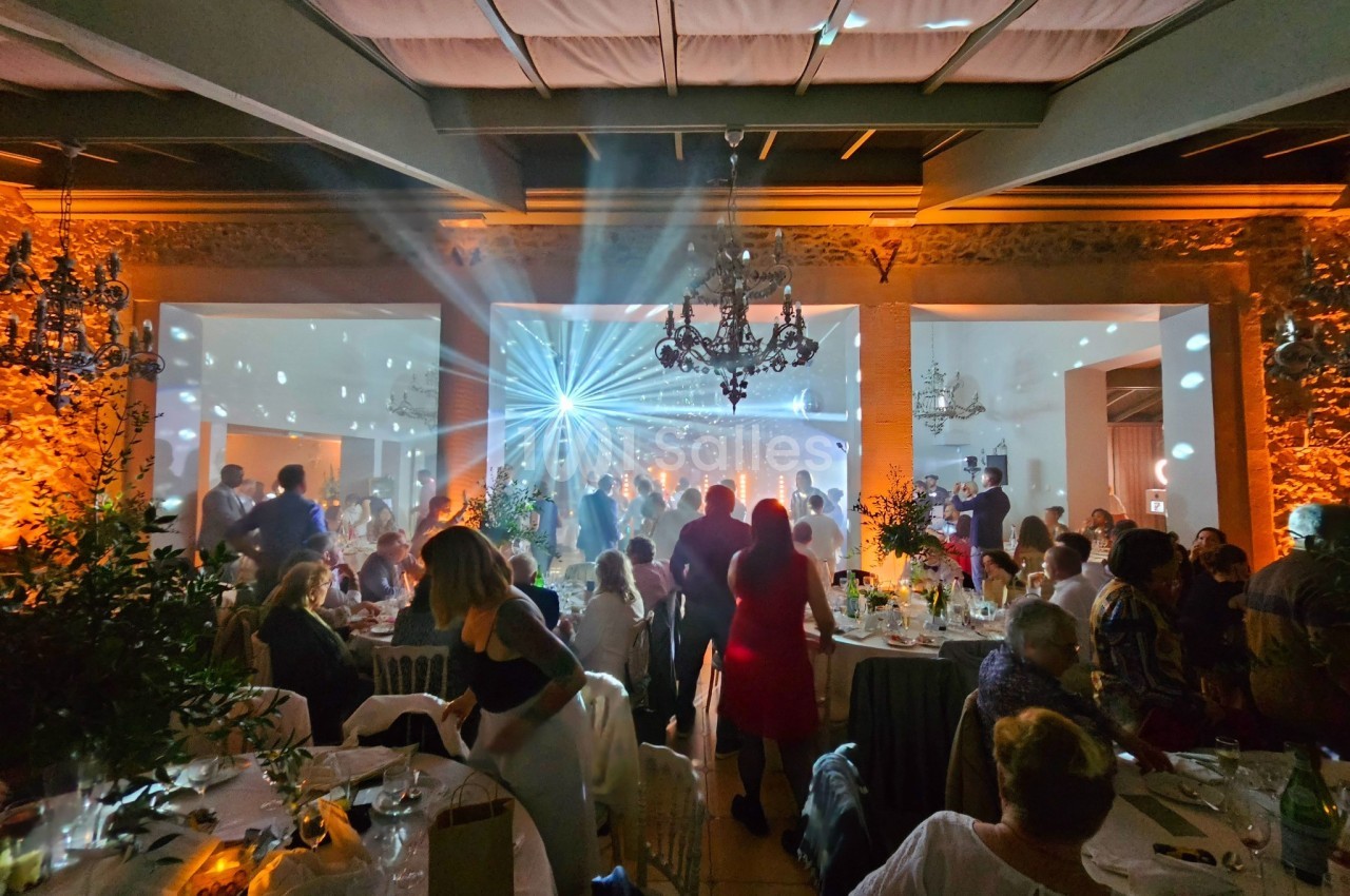 Salle de réception animée avec des invités dansant sous des jeux de lumière colorés et une ambiance festive.