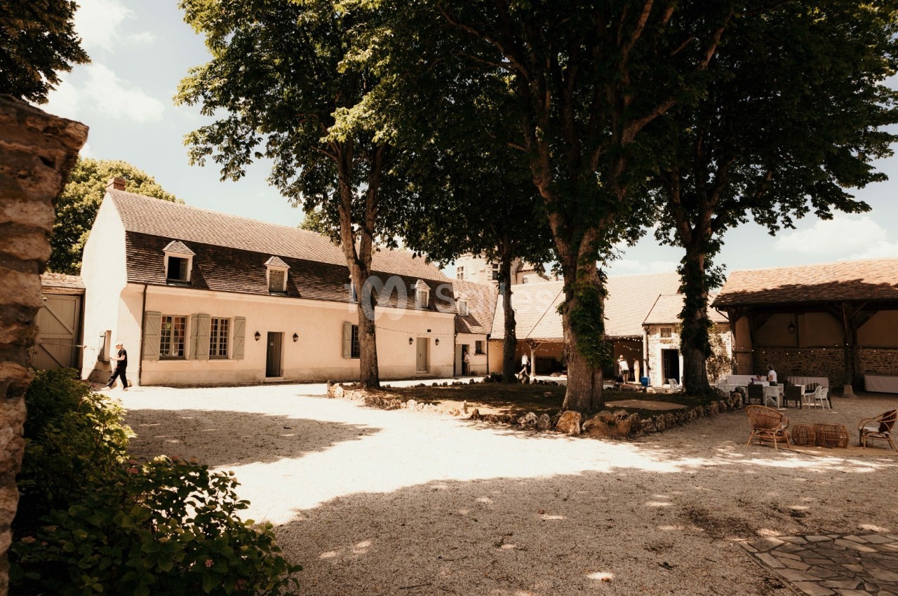 Cour intérieure avec une maison en pierre, des arbres ombrageant l'espace et quelques meubles d'extérieur.