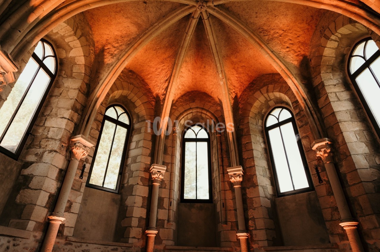 Intérieur d'une chapelle avec des fenêtres en ogive, des murs en pierre et un éclairage chaleureux.