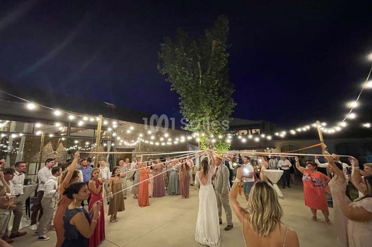 Des invités dansent autour d'un couple sous des guirlandes lumineuses, tenant des rubans reliés à un arbre.