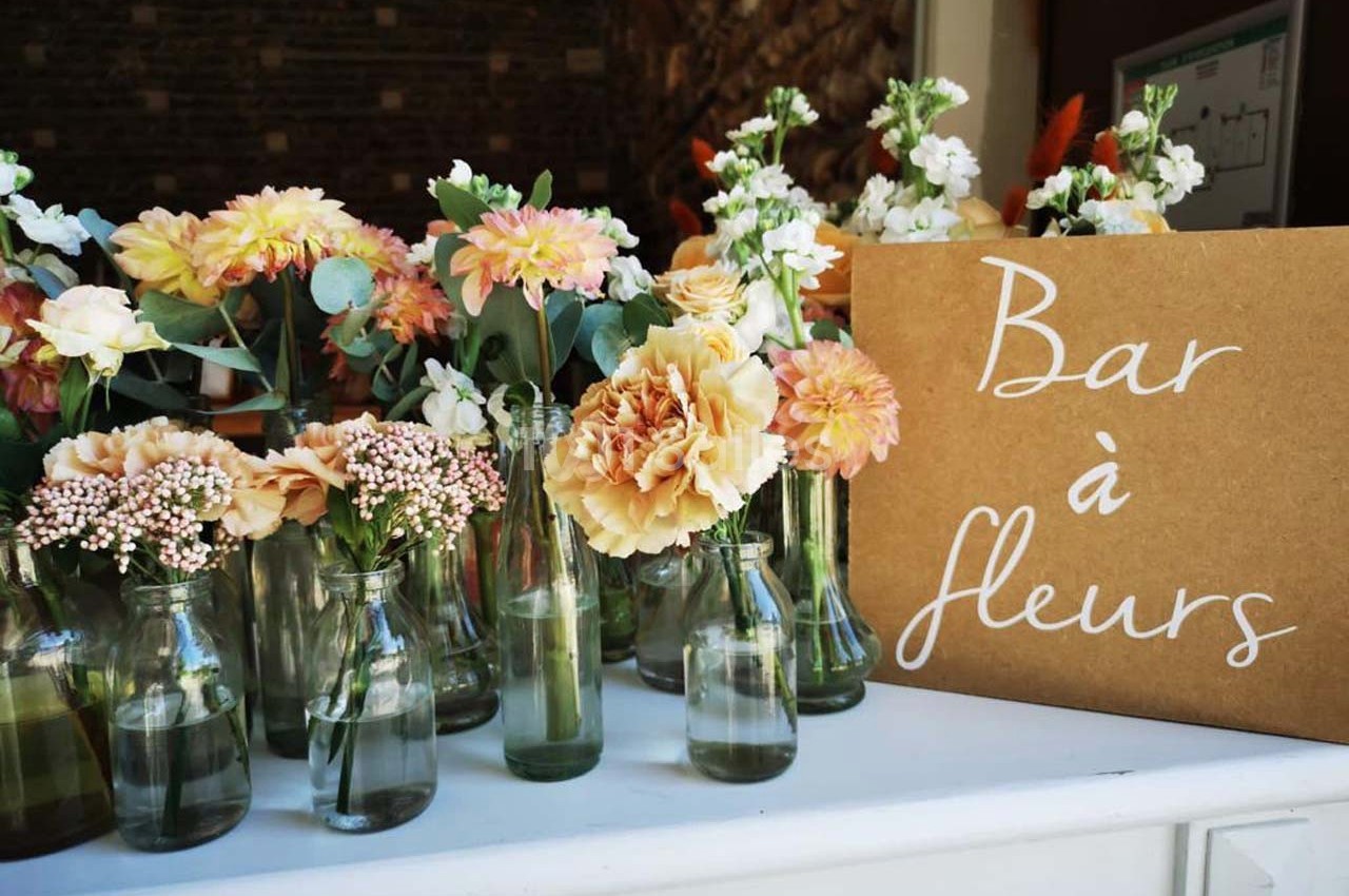 Des petits bouquets de fleurs variées dans des bouteilles en verre, avec une pancarte indiquant ’Bar à fleurs’.