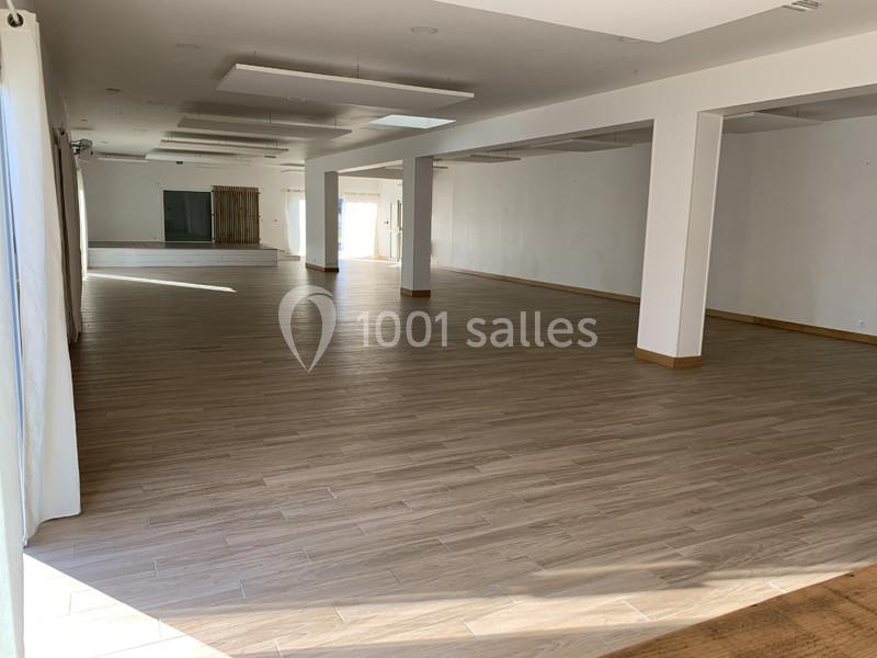 Salle spacieuse et lumineuse avec parquet en bois clair, murs blancs et grandes fenêtres laissant entrer la lumière…