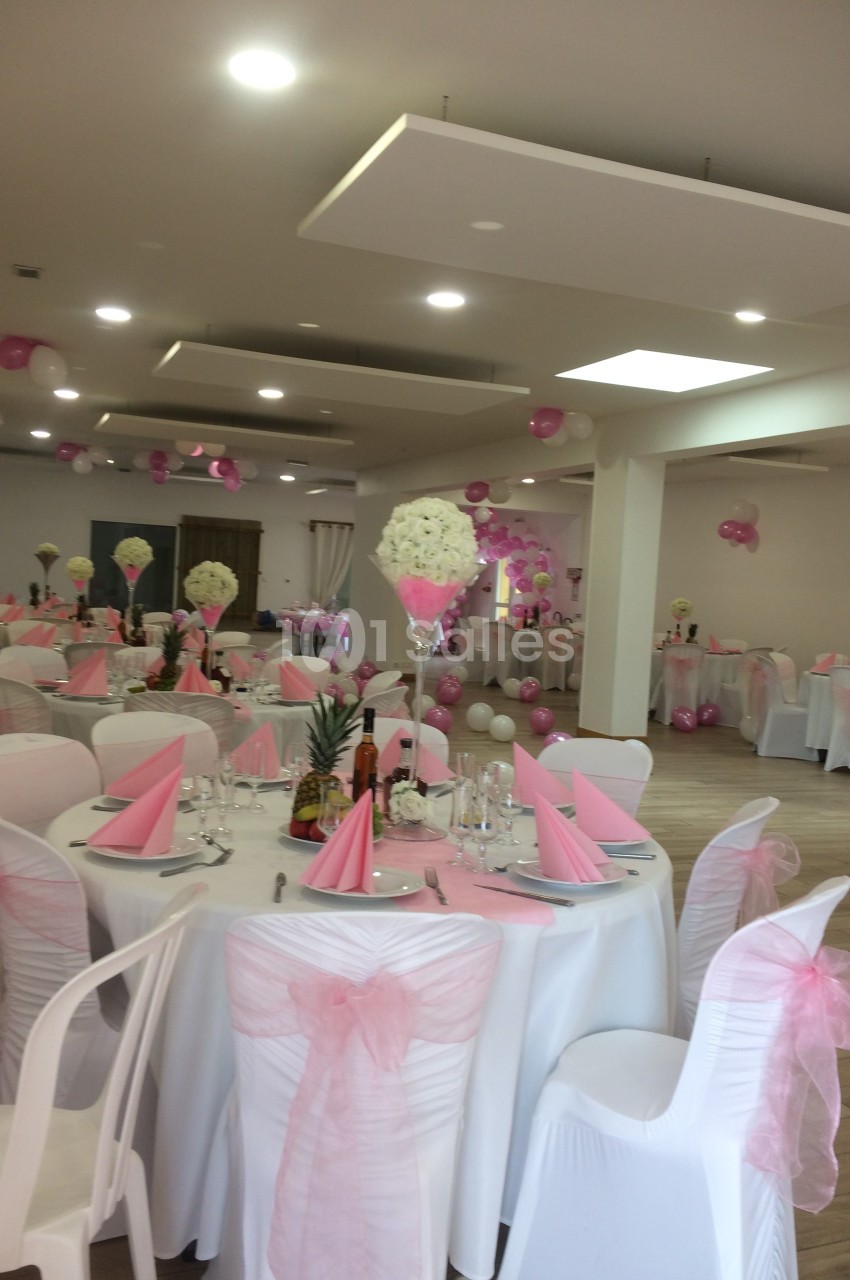 Salle de réception décorée avec des nappes blanches, des serviettes roses et des ballons assortis pour un événement festif.