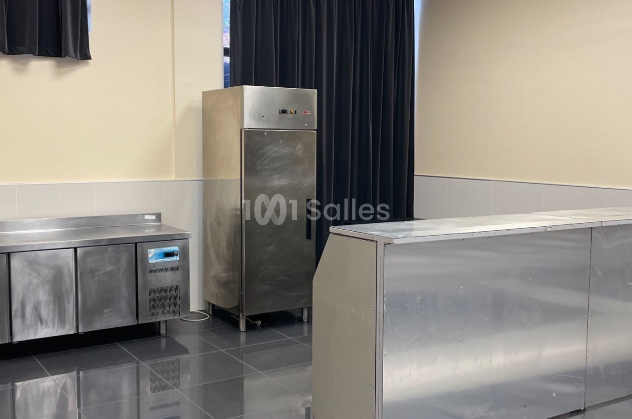 Cuisine professionnelle avec plan de travail en inox, armoire réfrigérée et murs clairs.