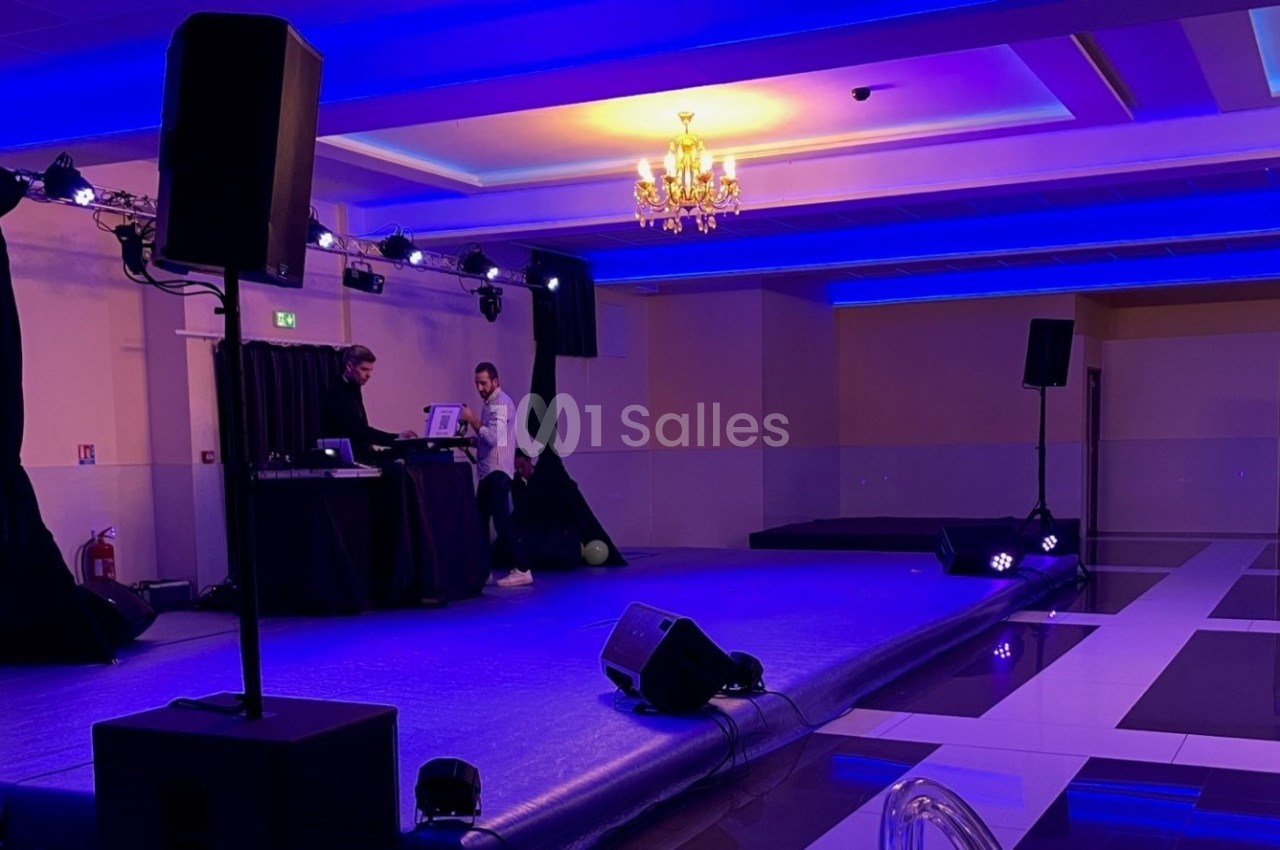 Salle de réception avec scène éclairée en bleu, équipement audio et deux personnes près d'une table de mixage.