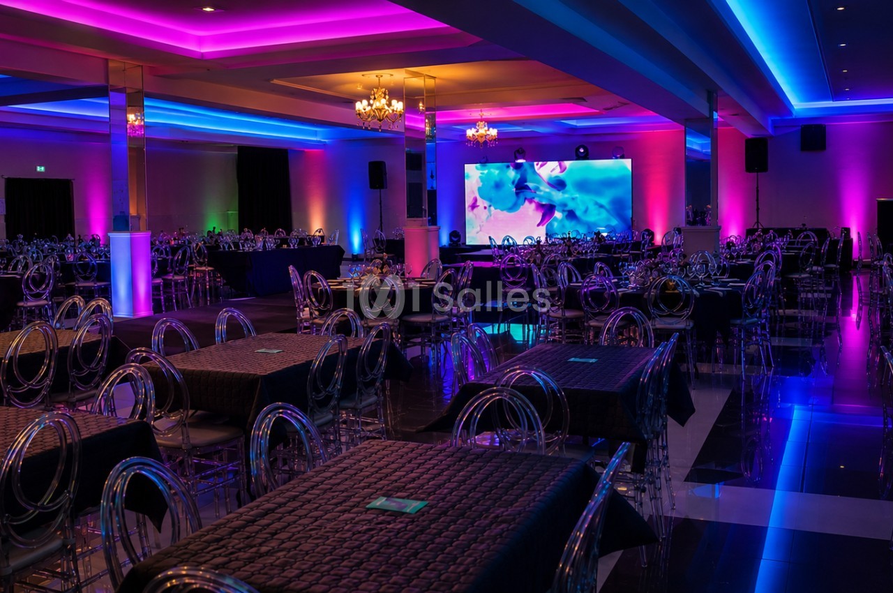 Salle de réception avec tables dressées, chaises transparentes et éclairage coloré violet et bleu.