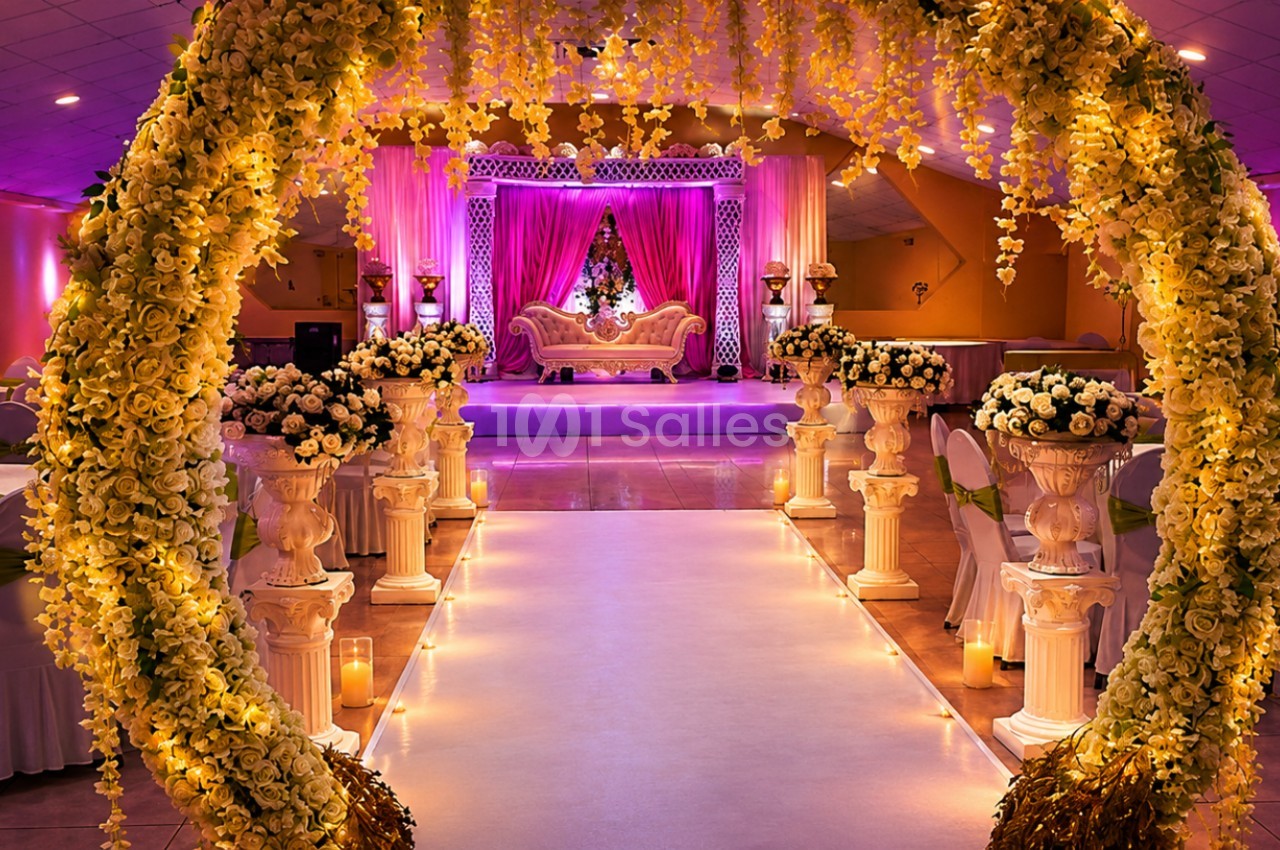 Salle de réception décorée avec des fleurs, un arc floral illuminé et une scène ornée d'un canapé élégant.