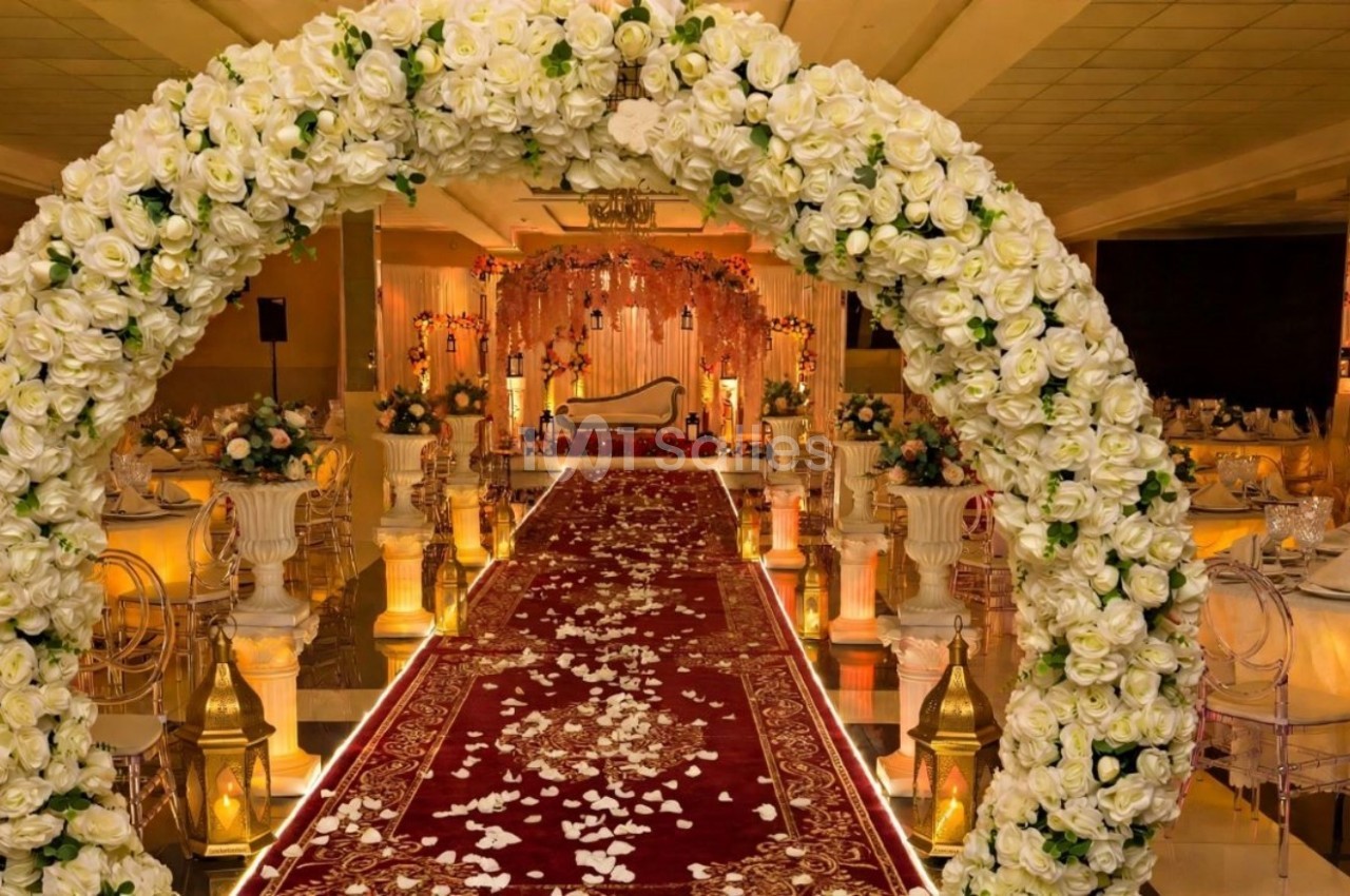 Arche de fleurs blanches encadrant une allée rouge décorée de pétales, menant à une scène ornée pour un événement.