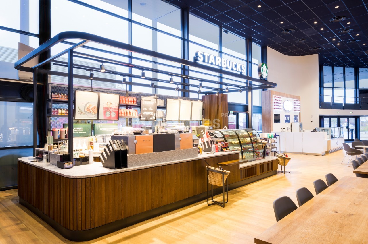 Comptoir de café moderne avec présentoirs de boissons et pâtisseries dans un espace lumineux et spacieux.